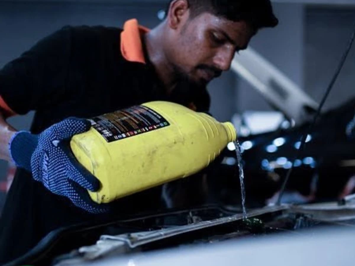 Technician pouring coolant from a yellow bottle into a car's engine bay