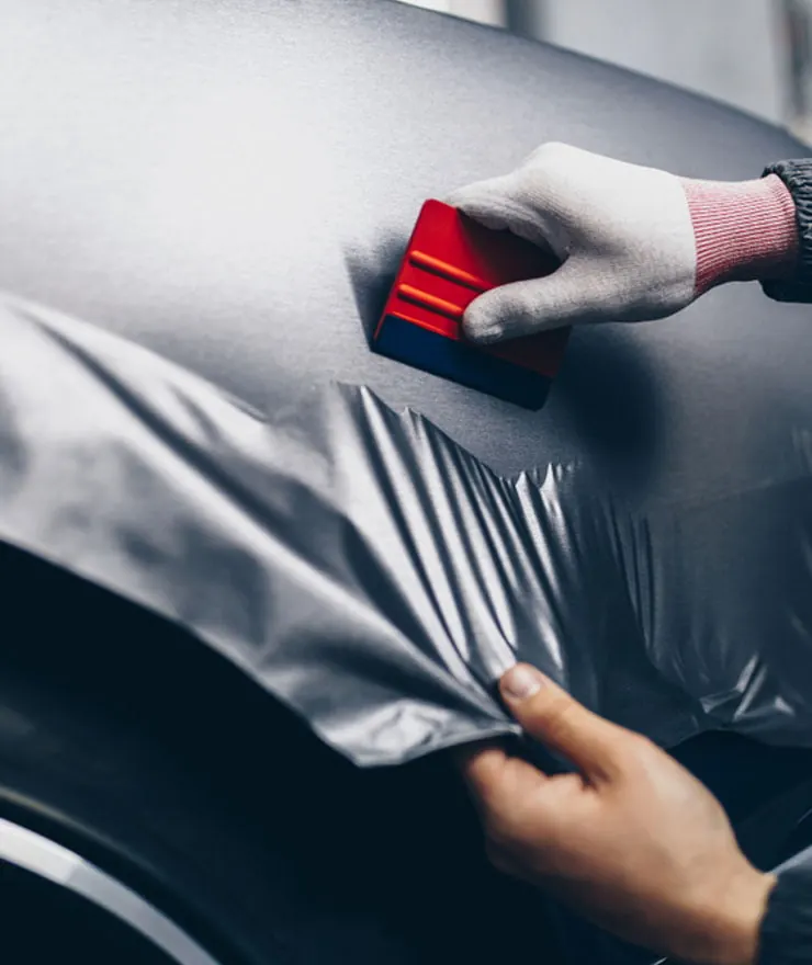 Gloved hand smoothing grey vinyl wrap onto a car panel with a squeegee