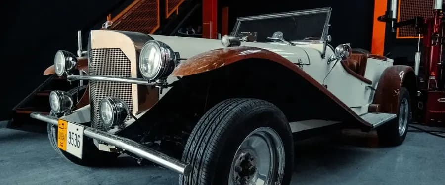 Cream vintage roadster with brown wings and chrome headlamps in a workshop